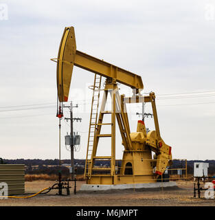 Large Yellow 912 Pump Jack on oil or gas well with surrounding equipment against an overcast sky Stock Photo