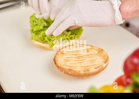 Chef adding lettuce leaf on burger. Stock Photo