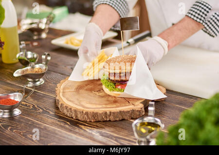 Chef adding french fries to burger. Stock Photo