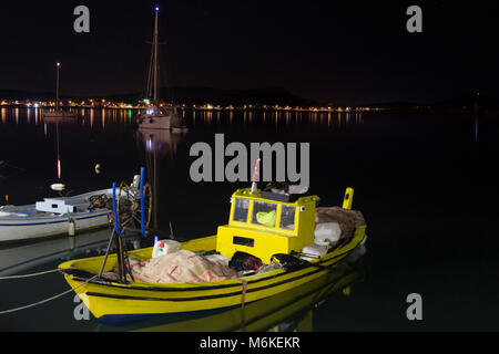 Small, wooden fishing boats with sailboats in the background in Cunda (Alibey) island ar night. Stock Photo