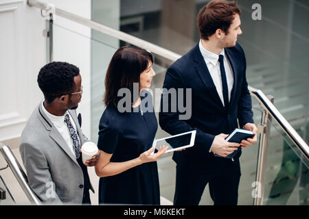 Three multiracial business people walking down on stairs with digital tablet Stock Photo