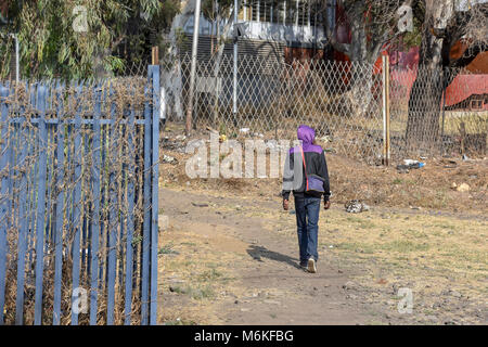 A male walking near a gate with barbed razor wire in Pretoria South Africa used as steel fencing constructed with sharp edges or points utilized to pr Stock Photo