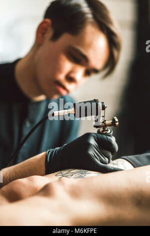 tattoo male artist makes a tattoo on a female leg. Stock Photo