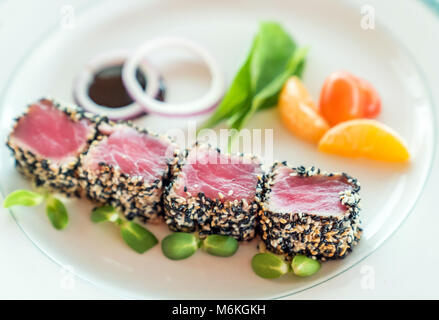 Seared tuna with sesame seeds with green salad on white plate Stock Photo