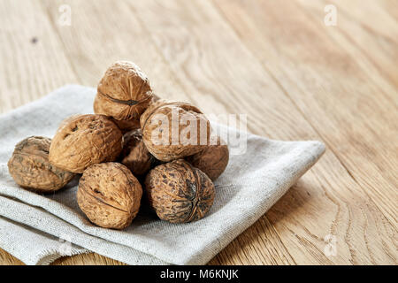 A stack of hard shells of walnuts piled together on light grey fabric cotton napkin and isolated on rustic wooden background, copy space, shallow dept Stock Photo