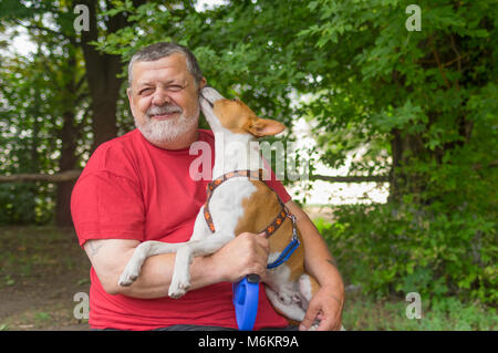 Bearded senior man taking young basenji that whisper in master's ear it loves him Stock Photo