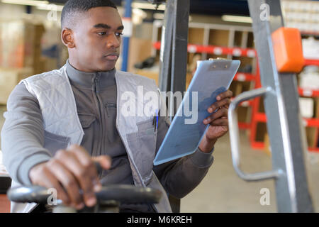 worker in logistics warehouse using a forklift checking list Stock Photo