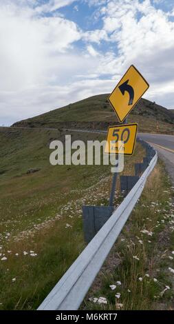 Winding two lane highway through Australian Alps region with yellow stripes, curve signs red snow poles and rolling hills and rounded mountains Stock Photo