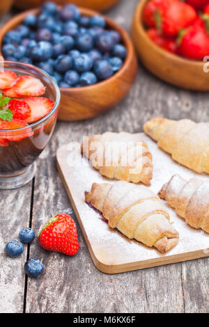 fresh  croissants and berries with cup of fruit tea on old wooden table Stock Photo
