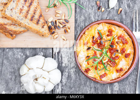 baked  camembert with chorizo garlic rosemary fryed pine nuts and toasted bread Stock Photo