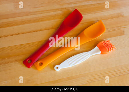 Beautiful new rubber accessories for baking on a wooden table. Silicone spatulas and brushes for cooking Stock Photo