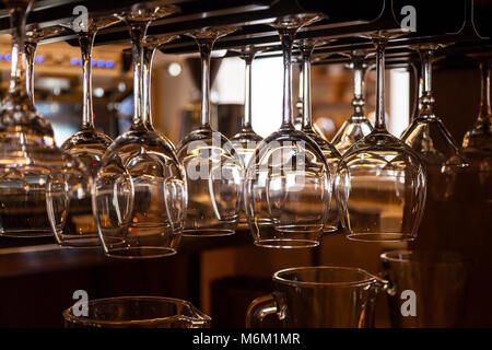 Beautiful new glasses for wine from glass hang in fastenings in even rows on a wooden table in a bar Stock Photo