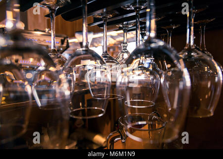 Beautiful new glasses for wine from glass hang in fastenings in even rows on a wooden table in a bar Stock Photo