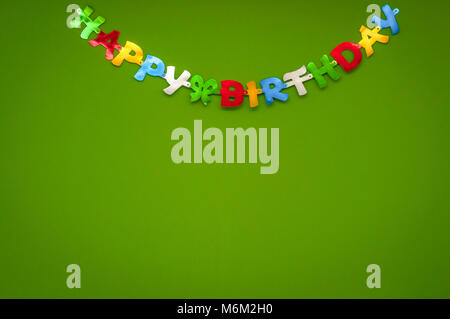 Colourful cheerful Happy Birthday greeting banner on a green wall in a celebration and party concept. Stock Photo