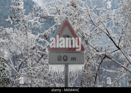 Road sign danger curve covered in ice after the freezing rain Stock Photo