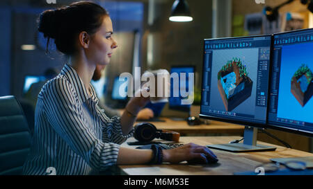 Female Game Developer Works on a Level Design on Her Personal Computer with Two Displays, She Works Late and Drinks Coffee. Creative Loft Office Stock Photo