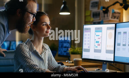 Female UX Architect Has Discussion with Male Design Engineer, They Work on Mobile Application Late at Night, She Drinks Coffee. Loft, modern office. Stock Photo