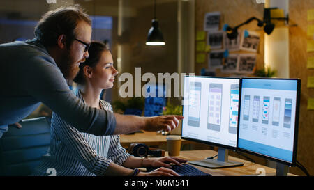 Female UX Architect Has Discussion with Male Design Engineer, They Work on Mobile Application Late at Night, She Drinks Coffee. Loft, modern office. Stock Photo