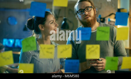 Male and Female Designers Discuss and Outline They're Project with Sticky Notes on a Glass Wall. They're Young and Creative People Who Work in Office Stock Photo