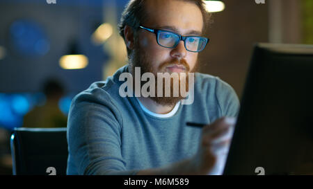 Talented Young Concept Artist Drawing on a Digital Pen Display Tablet While Sitting at His Working Place in Modern Loft Office. Late at Night. Stock Photo