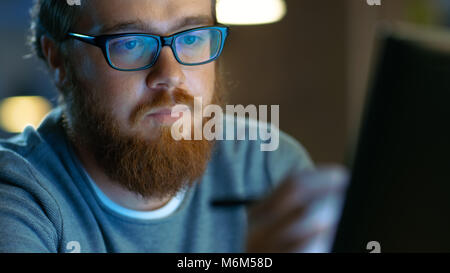 Talented Young Concept Artist Drawing on a Digital Pen Display Tablet While Sitting at His Working Place in Modern Loft Office. Late at Night. Stock Photo