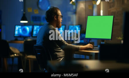 Creative Bearded Man Works on a Personal Computer with Isolated Mock-up Green Screen. He Works Alone in the Office Late at Night. Stock Photo