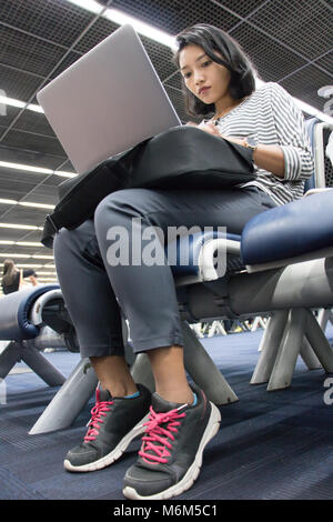 A young woman is working on a computer in an airport lobby while waiting for her  depart. Stock Photo