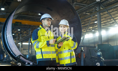 Male and Female Industrial Engineers Have Discussion while Using Tablet Computer. They Work in a Heavy Industry Manufacturing Factory. Stock Photo
