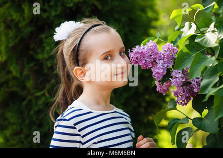 Little girl smelling lilacs in the garden. Beautiful spring day. Selective focus. Stock Photo