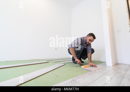 carpenter worker installing wood parquet board during flooring work with hammer Stock Photo