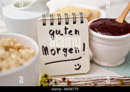closeup of a table set for breakfast with a porcelain bowl with cereals, some toasts, a bowl with jam and a note with the text guten morgen, good morn Stock Photo