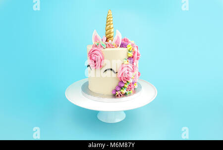 Unicorn buttercream cake on white cake stand on turquoise background Stock Photo