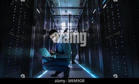 IT Technician Works on Laptop in Big Data Center full of Rack Servers. Multiple People Works at Data Center at the same time. Stock Photo