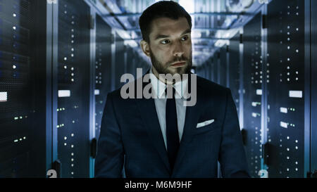 Businessman Walking Through Data Center Corridor  with Server Rack Visually Inspecting Working Server Cabinets. Stock Photo