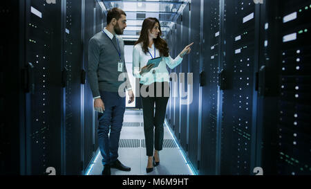 Female and Male IT Engineers Discussing Technical Details in a Working Data Center/ Server Room. Stock Photo