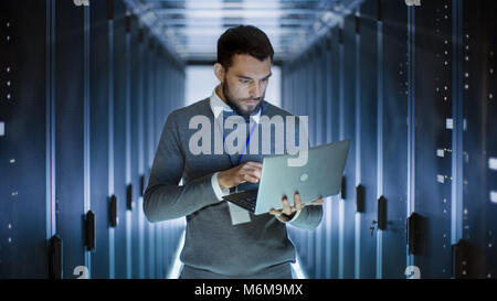 Male Server Engineer Works on a Laptop in Large Data Center. Stock Photo