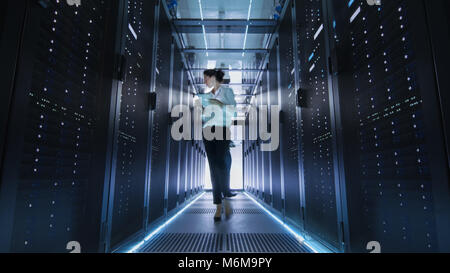 Female IT Engineer Walking through Data Center Corridor. She is Holding Tablet Computer. She is Blurred in Motion. Stock Photo