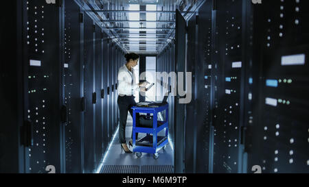 Female IT Engineer Works on a Laptop and Scans and Swaps Hard Drives That are Lying on a Cart. She Works in Data Center. Stock Photo