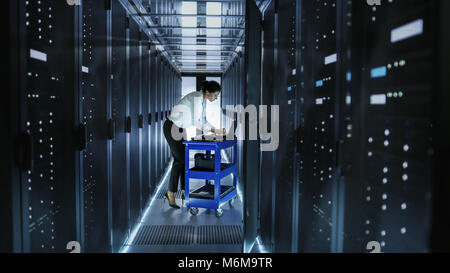 Female IT Engineer Works on a Laptop and Scans and Swaps Hard Drives That are Lying on a Cart. She Works in Data Center. Stock Photo