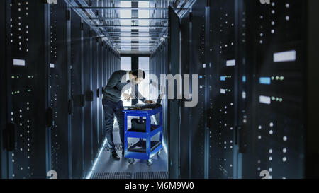 IT Engineer Works on a Laptop and Scans Hard Drives That are Lying on a Crash Cart. He Works in Data Center. Stock Photo