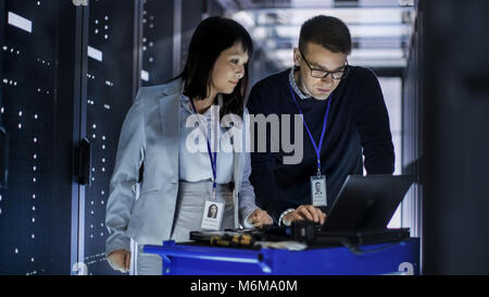 Caucasian Male and Asian Female IT Technicians Working with Computer Crash Cart in Big Data Center full of Rack Servers. Stock Photo