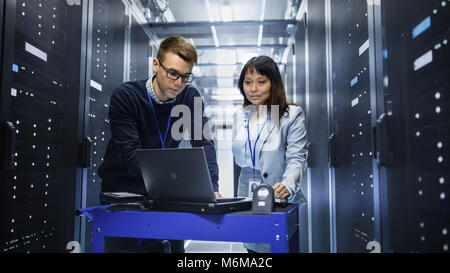 Caucasian Male and Asian Female IT Technicians Working with Computer Crash Cart in Big Data Center full of Rack Servers. Stock Photo