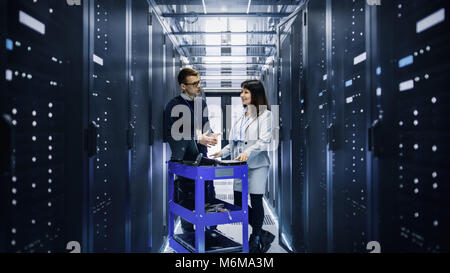 Caucasian Male and Asian Female IT Technicians Working with Computer Crash Cart in Big Data Center full of Rack Servers. Stock Photo