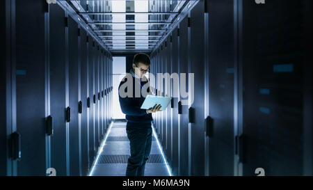 Male IT Engineer Works on a Laptop in front of Server Cabinet at a Big Data Center. Rows of Rack Servers are Seen. Stock Photo