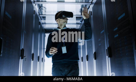 IT Engineer Wearing Virtual Reality Headset Works with Augmented Reality Software in Data Center. He Wirelessly Interacts with Rack Servers. Stock Photo