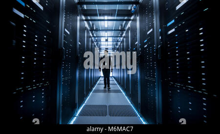 Shot of IT Engineer Walking Through Data Center Corridor with Rows of Rack Servers. Stock Photo