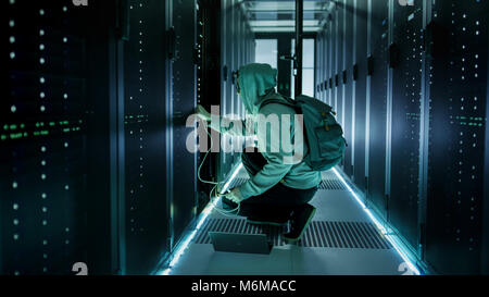 A Hooded Hacker With Laptop Connects to Rack Server and Steals Information from Corporate Data Center. Stock Photo