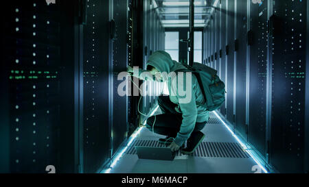 A Hooded Hacker With Laptop Connects to Rack Server and Steals Information from Corporate Data Center. Stock Photo