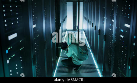 A Hooded Hacker With Laptop Connects to Rack Server and Steals Information from Corporate Data Center. Stock Photo
