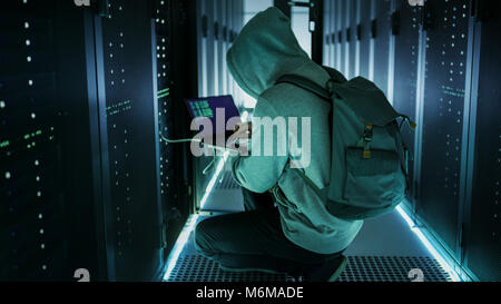A Hooded Hacker With Laptop Connects to Rack Server and Steals Information from Corporate Data Center. Stock Photo